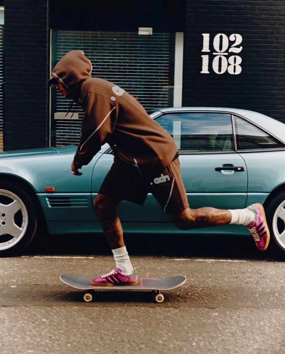 Persona en patineta con hoodie y short café, junto a un carro verde
